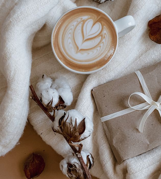 Imagen desde arriba café con espuma y decoración, un ramo de algodón y un paquete envuelto en papel craft con un lazo